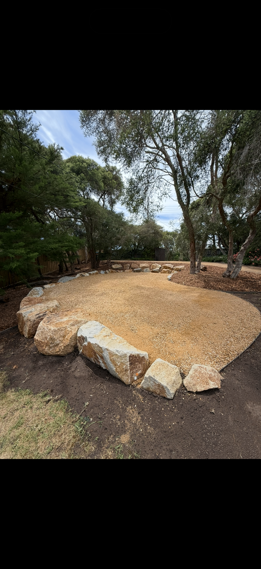 Fresh crushed granite pad edged with feature boulders under established coastal tea trees.
