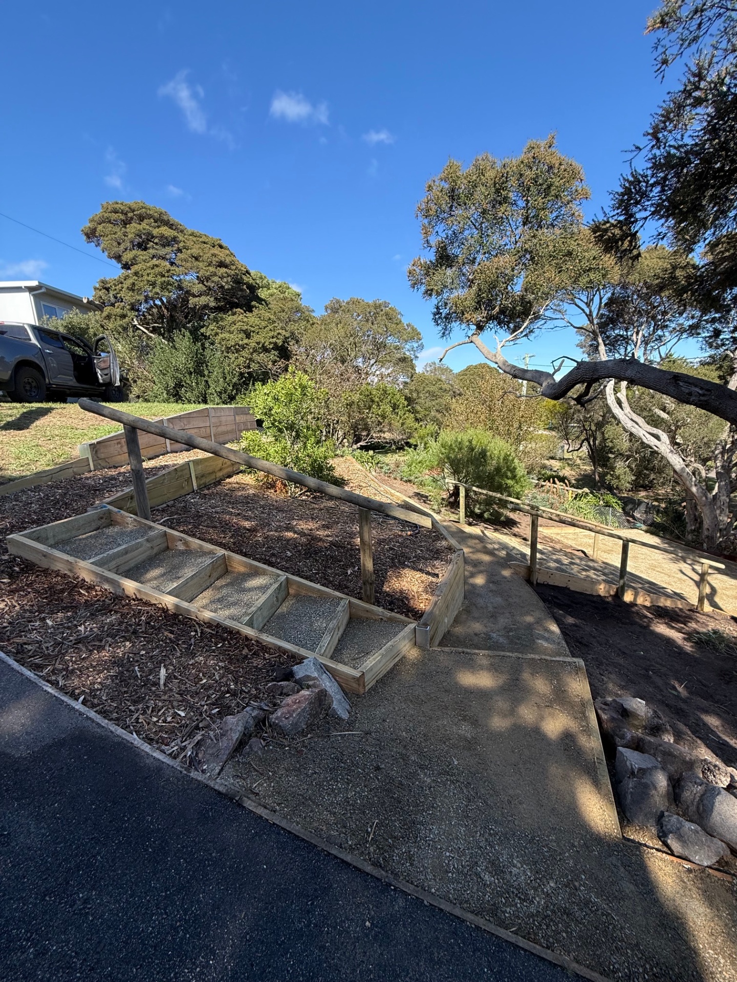 New treated pine steps and retaining walls cut into a coastal slope beside a fresh gravel path.